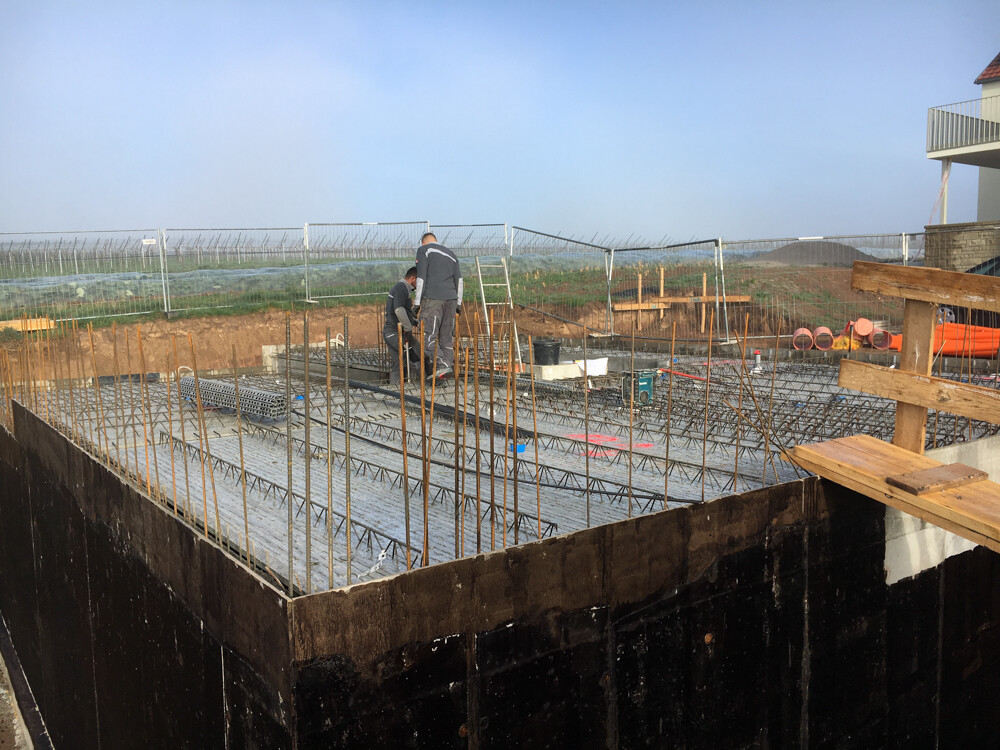 Construction workers working on a foundation slab with steel reinforcement bars; outdoor construction site