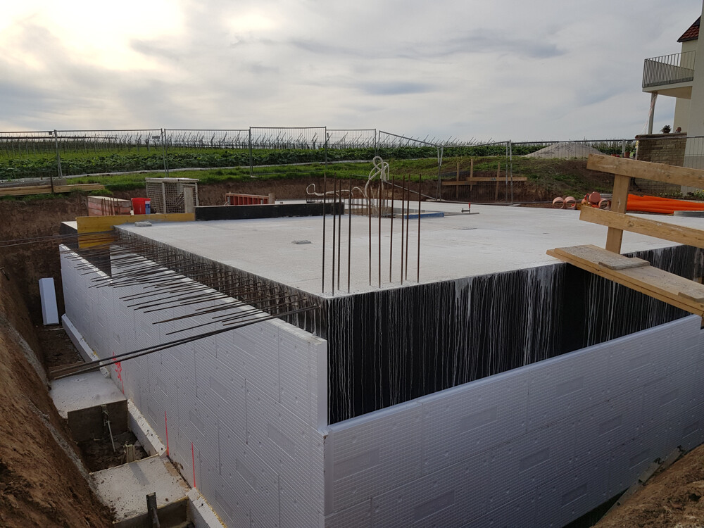 Foundation slab with vertical steel reinforcement, insulated block wall, excavation pit and wooden scaffolding.