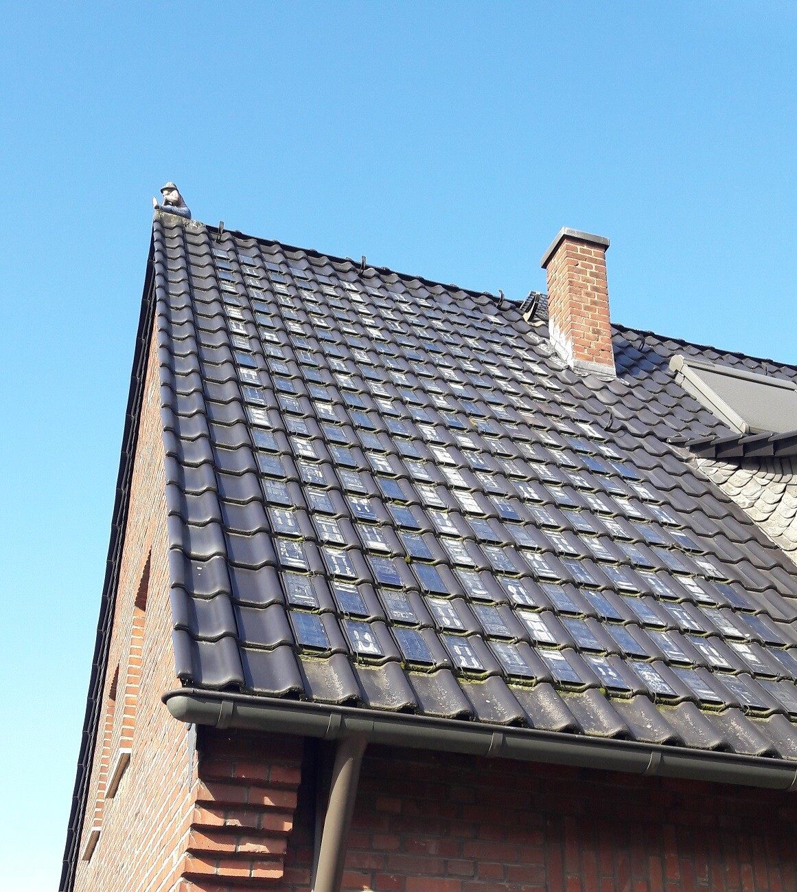 Gable roof with dark roof tiles, red chimney and blue sky.