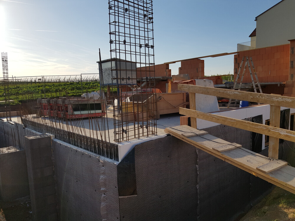 Construction site with foundation, steel reinforcement, brick walls and temporary wooden bridge.