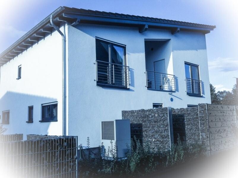 White, two-story house with two balconies, metal railings, fence, and garden.