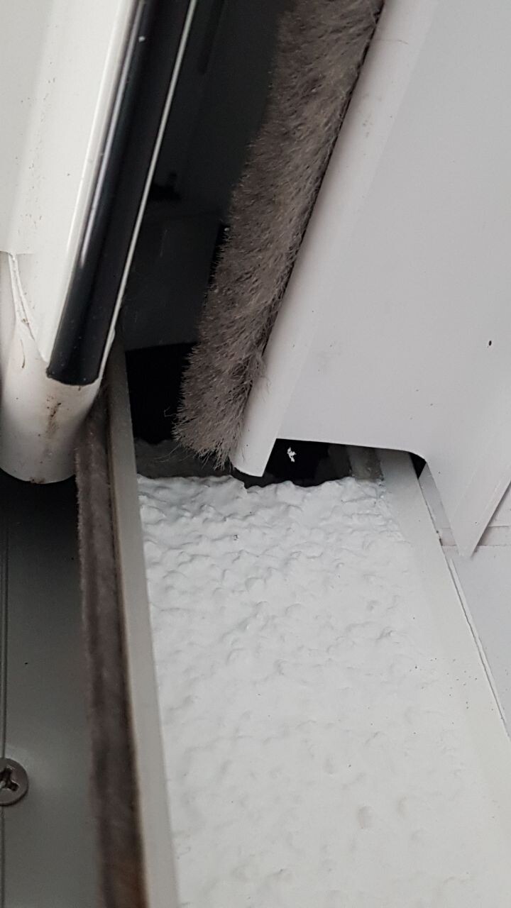 Close-up of a window frame with damaged seal and insulation