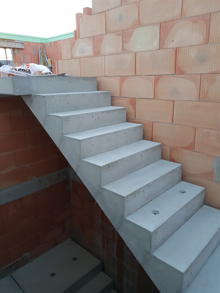 Concrete staircase in shell construction next to red brick masonry; unfinished building structure visible.