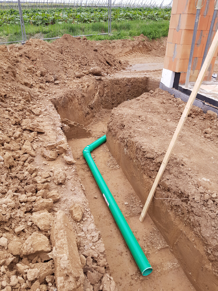 Trench with green PVC pipe in an excavation pit next to the house foundation.