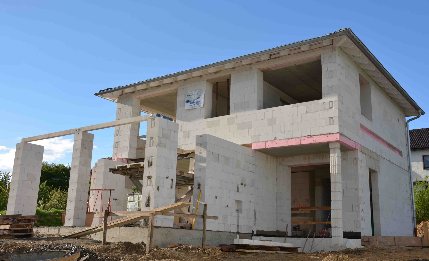 Shell construction of a two-story house made of concrete blocks with open window openings and wooden scaffolding
