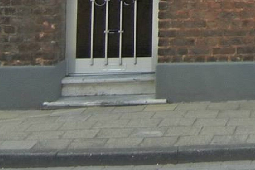 Exterior view of a house entrance with steps, metal door, and brick wall