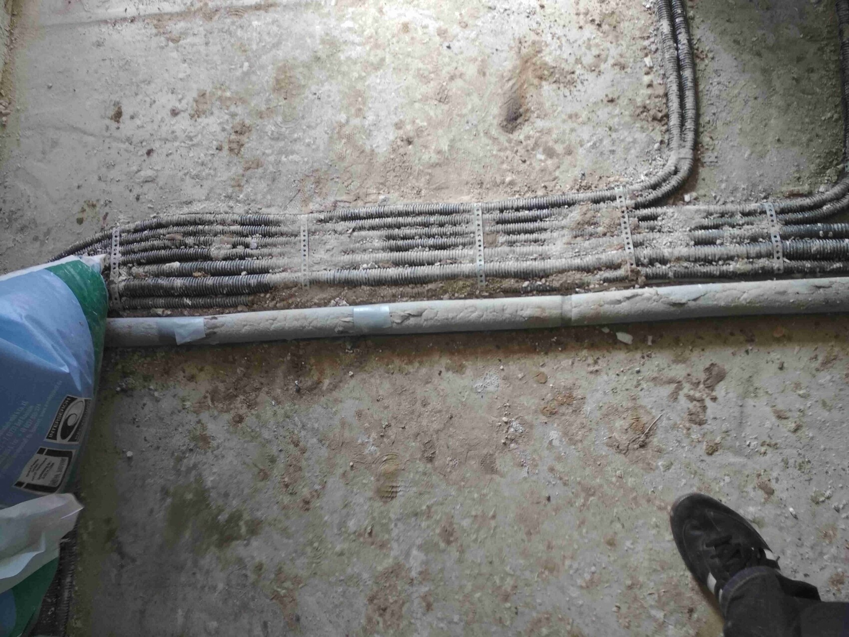 Construction site with installed electrical conduits on the floor, shoe visible at bottom edge