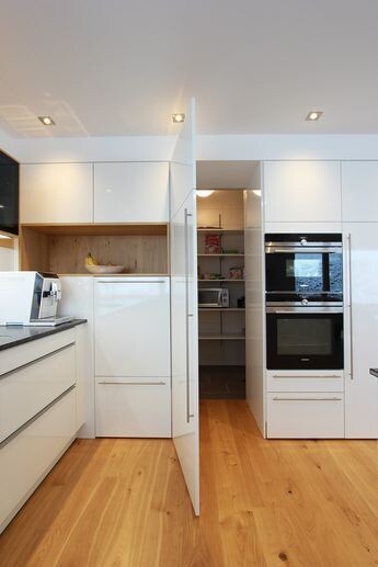 Modern white kitchen with wooden floor, integrated ovens and open pantry.