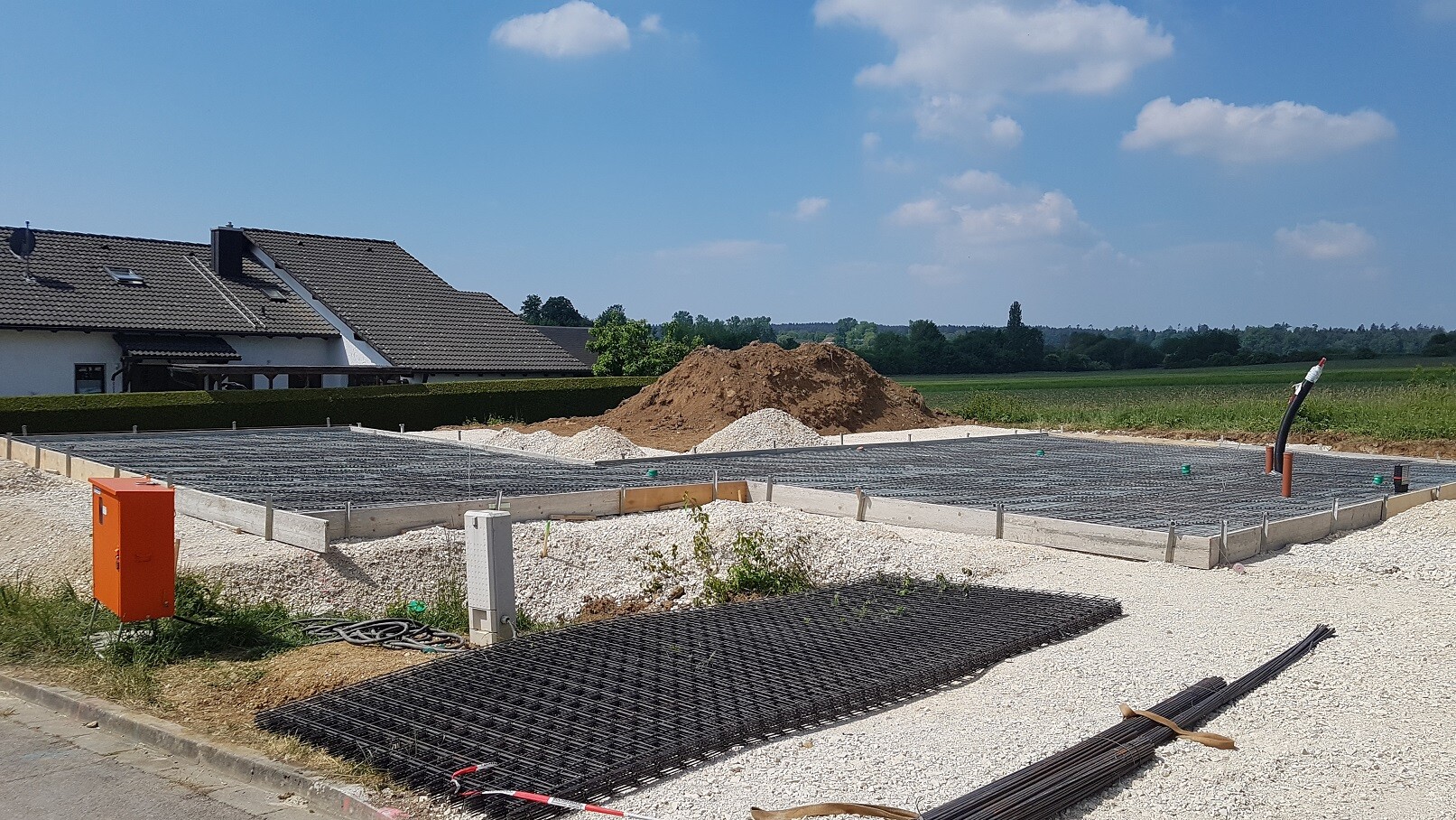 Foundation construction site with reinforcement steel mesh, gravel, and adjacent house
