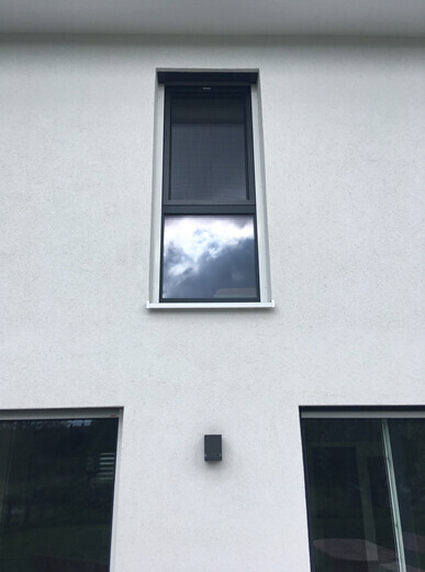 Exterior facade of a residential building with a top window, two side windows, and a wall lamp.