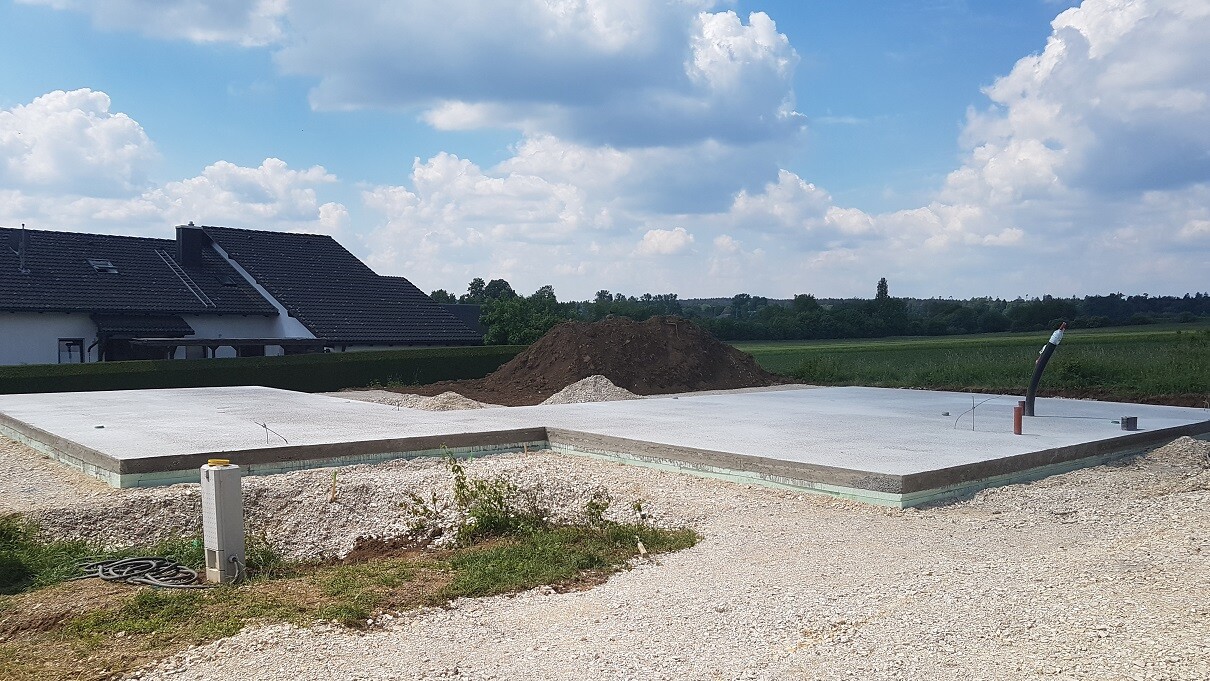Foundation slab on a new build construction site with soil, earth, and neighboring residential houses.