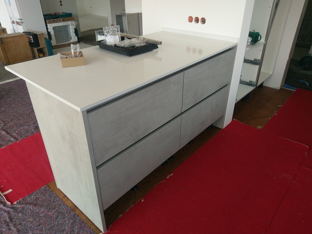 White kitchen island with six gray drawers, installed in a workshop.