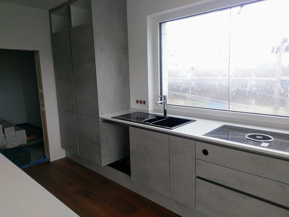 Modern kitchen with light grey fronts, sink, induction cooktop, and large window.