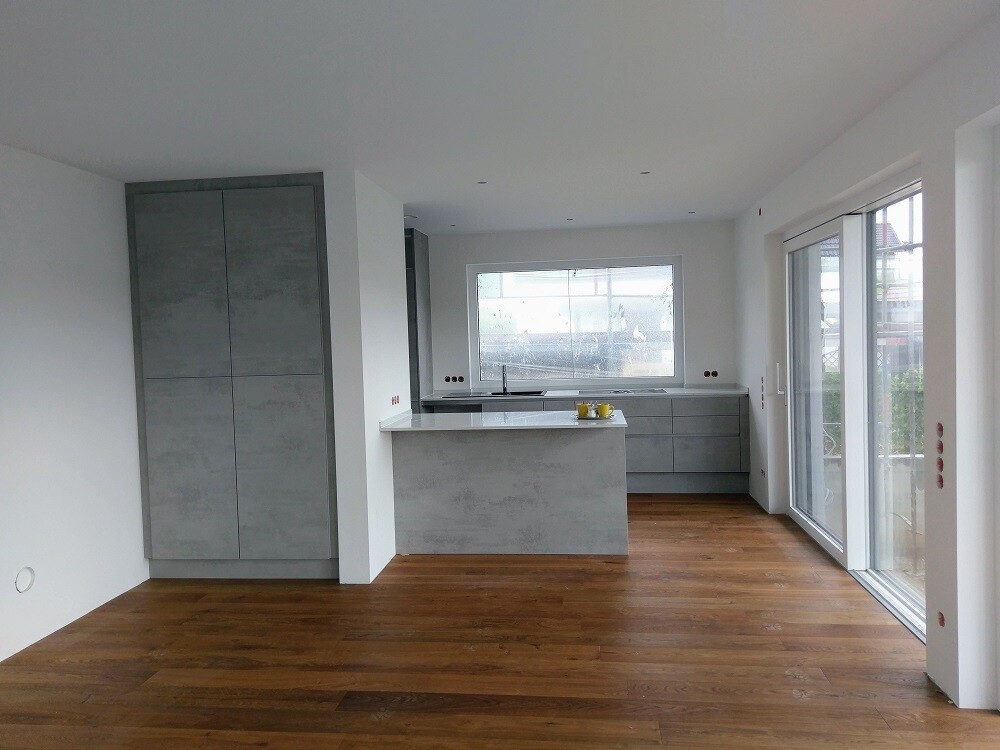 Modern kitchen with grey fronts, island, wood flooring, and large window front.