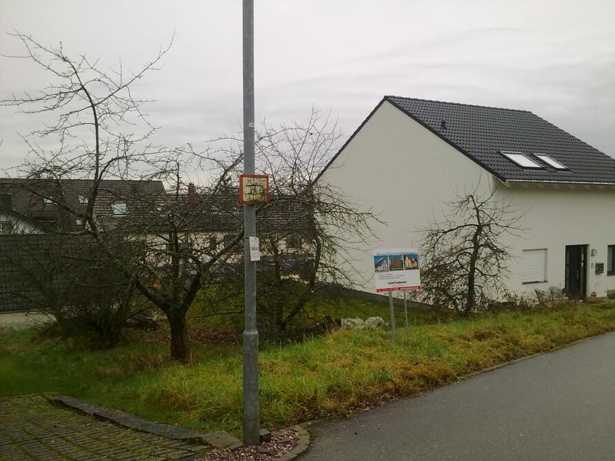 White single-family house street view with gable roof, trees and sign in the foreground.