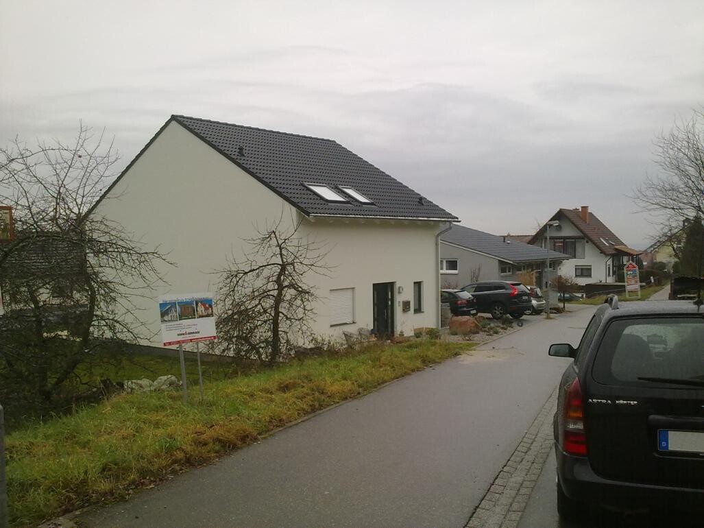 Row of white modern houses with gray pitched roofs and parked cars on the street.