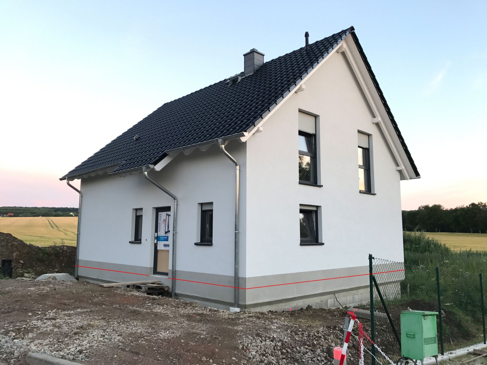 White detached house with dark pitched roof, building zone in front, rural fields in the background