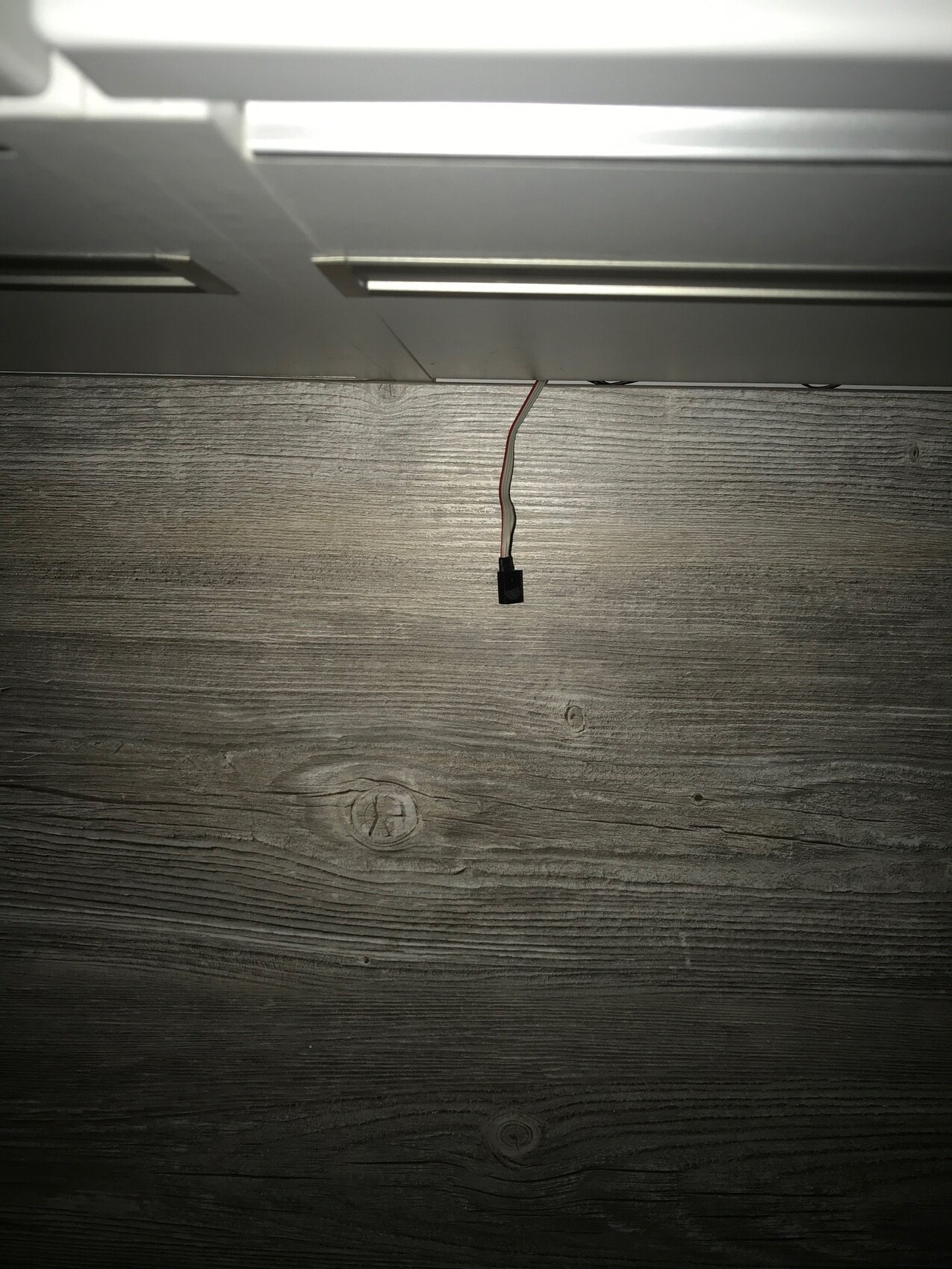 Hanging cable with black connector over wooden floor under white furniture piece.