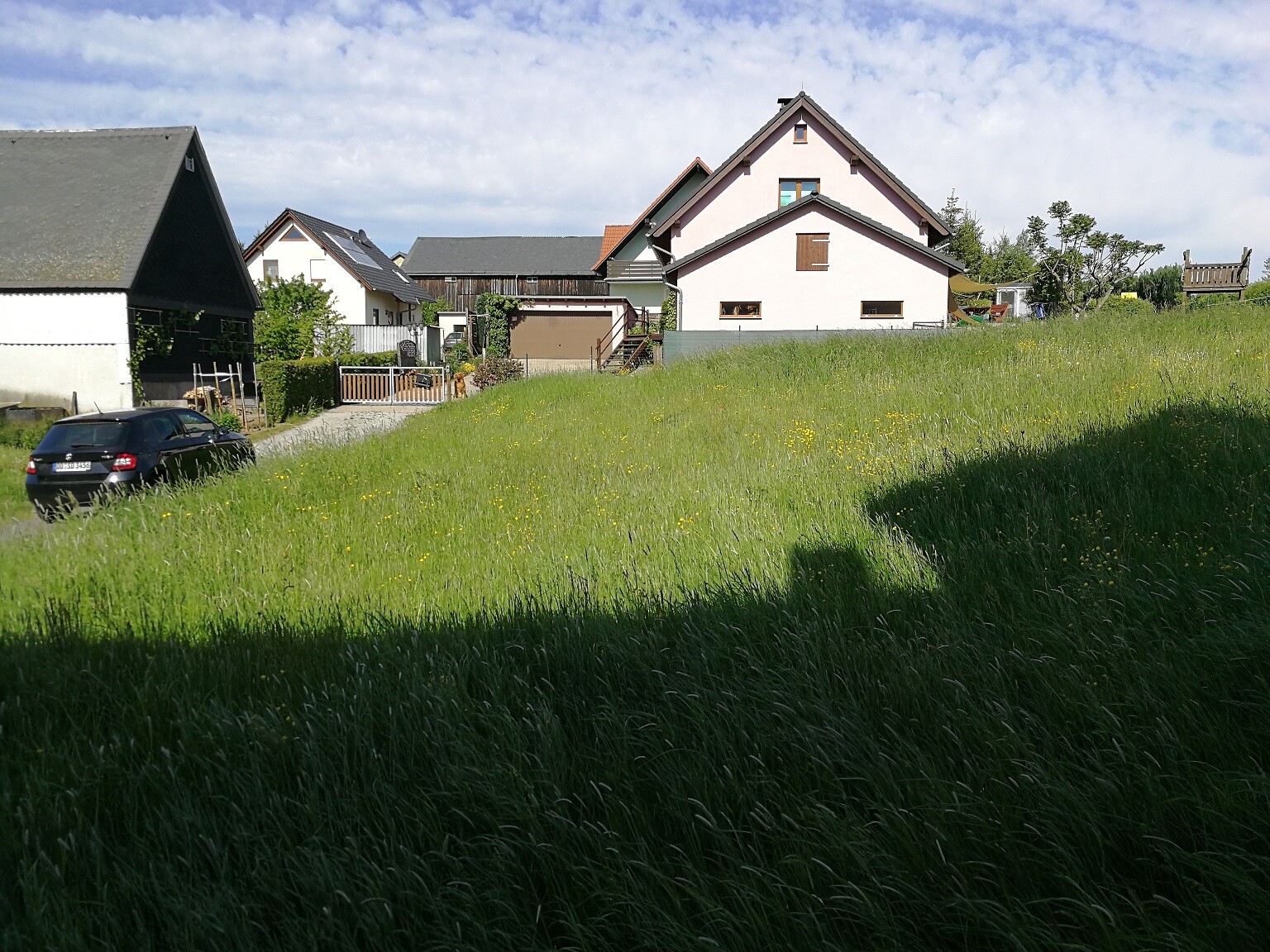 Gruenes-grasfeld-vor-haeusern-mit-parkendem-auto-und-blauem-himmel