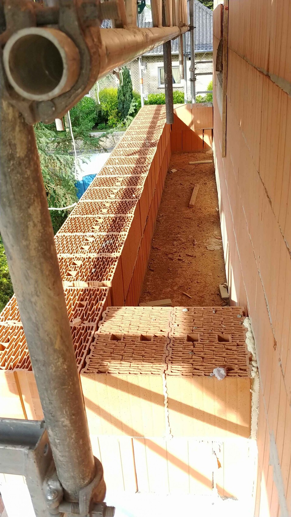 Construction site: orange brick wall, perforated bricks resting on the scaffolding, narrow walkway.