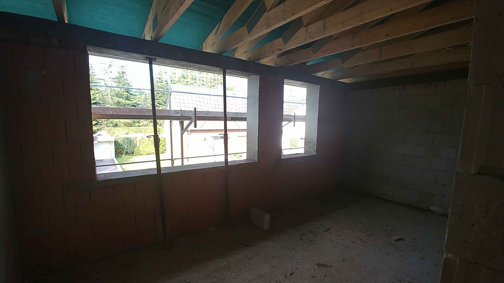 Unfinished interior of a new build with block walls, wooden beam ceiling, and scaffolding in front of windows