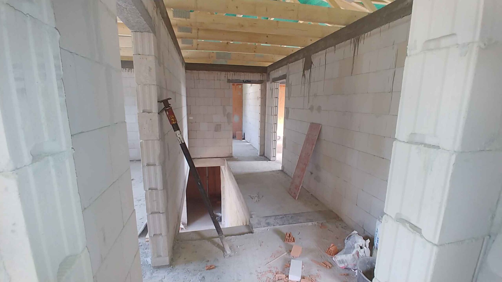 Unfinished interior on a construction site: white blocks, wooden ceiling, open stairwell, construction debris