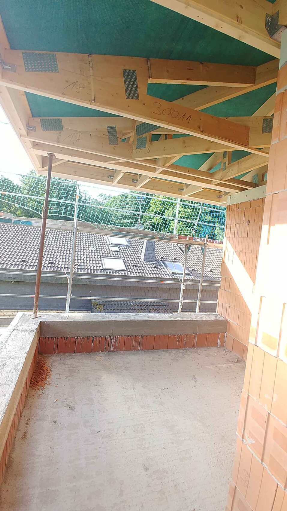 Shell of a balcony with wooden roof frame, green insulation boards, and scaffold netting.