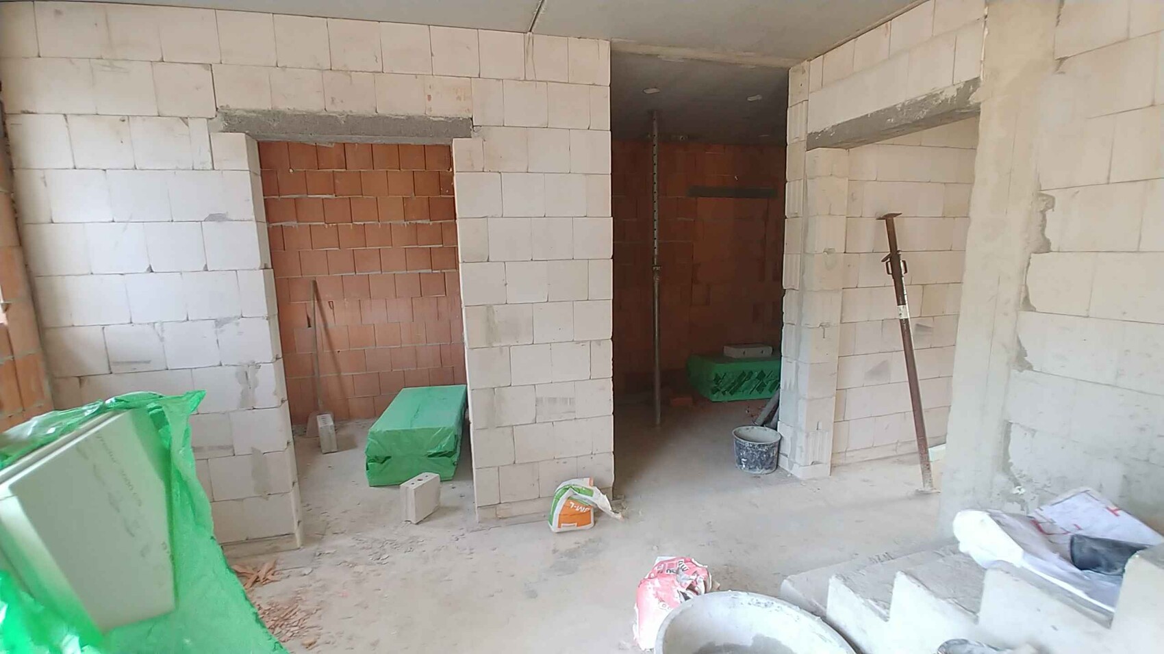 Interior of a construction site: white concrete blocks, orange brick walls, buckets and materials.