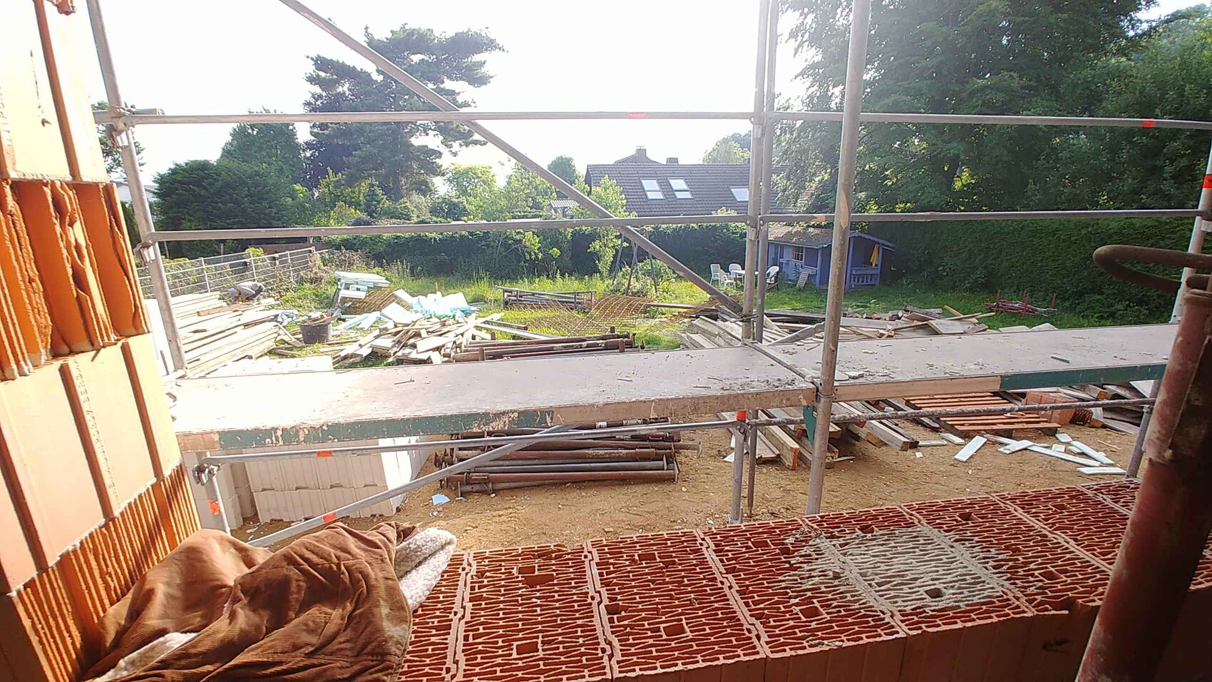 Construction site with scaffolding and wood piles; view from the balcony to the garden and house in the background