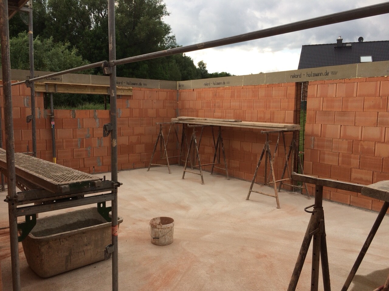 Construction site: Interior with red brick walls, scaffolding, saw horses, wooden planks, bucket