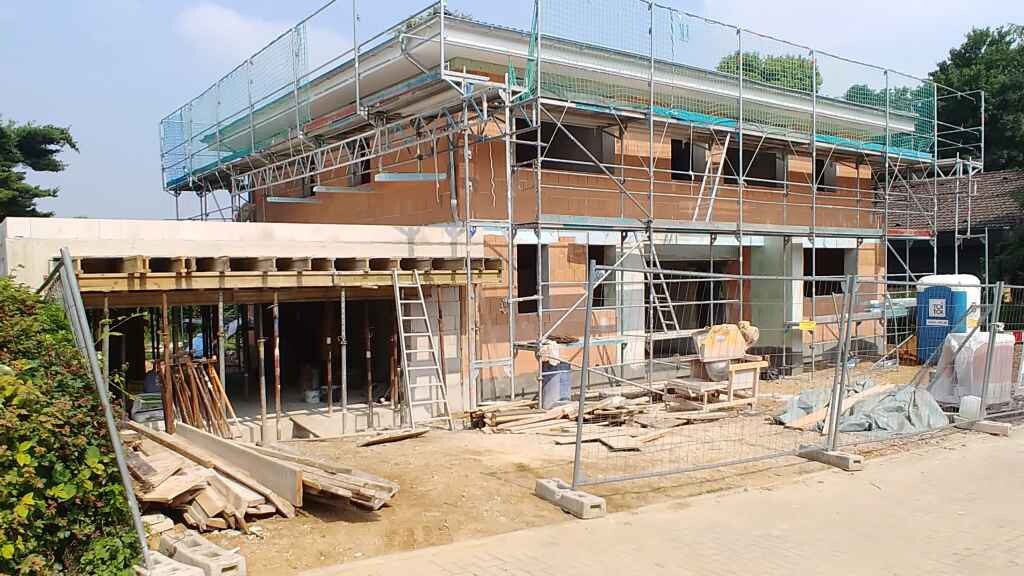 Two-story shell construction with scaffolding and building lumber at a construction site.