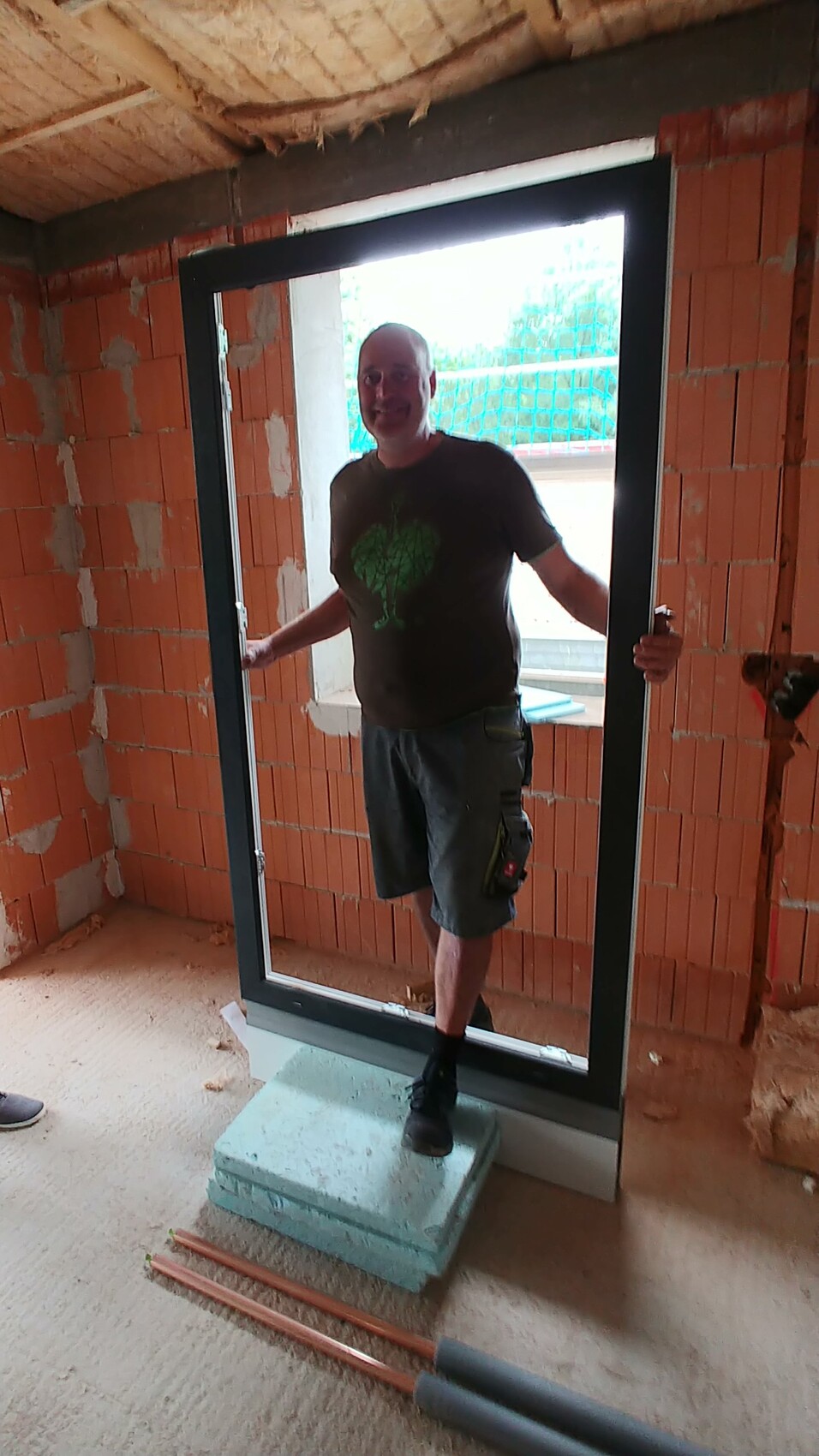 Man standing in a newly installed door frame of a shell construction, construction site visible.