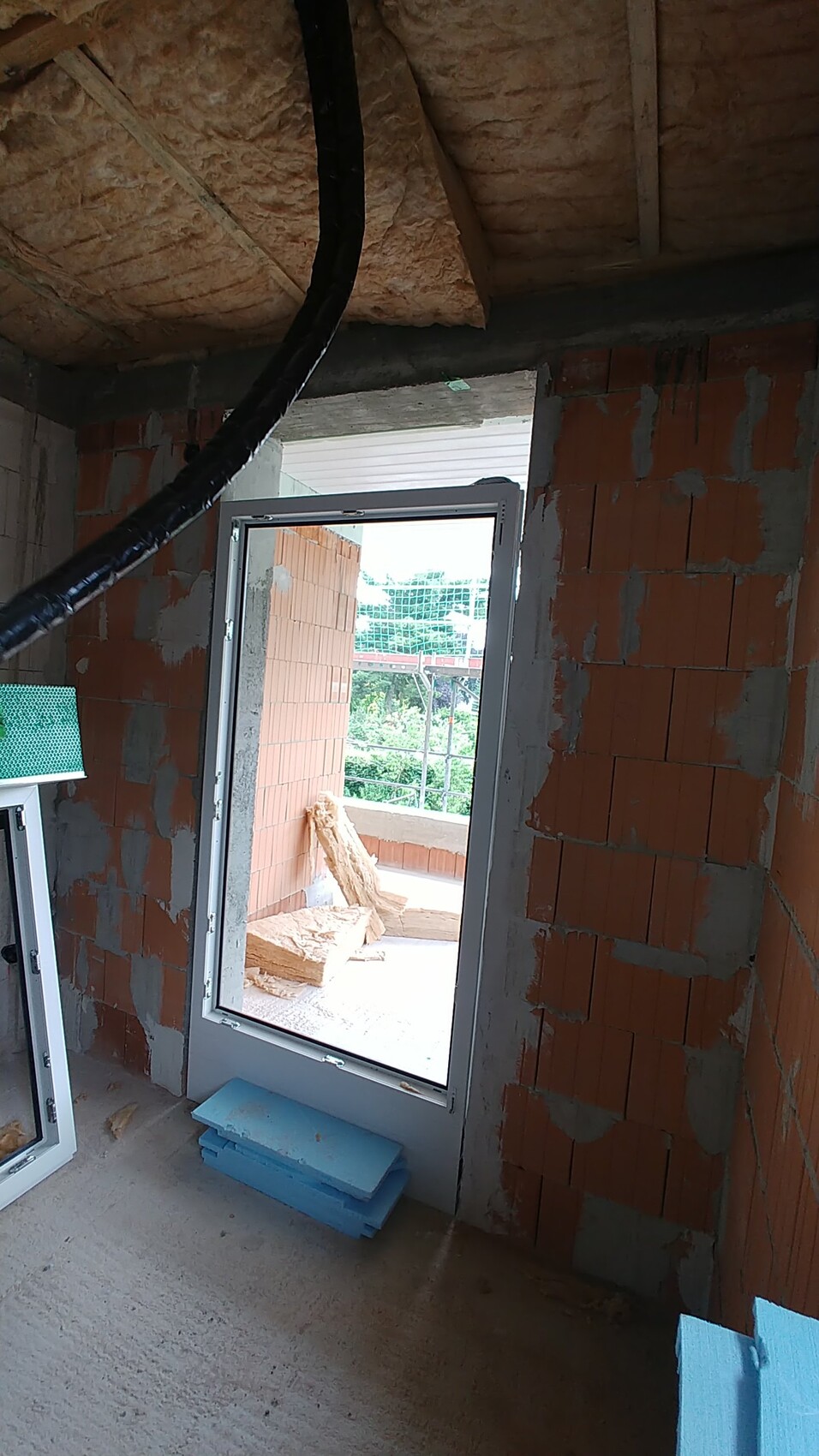 Unfinished interior in shell construction with brick walls, open door to balcony, and insulation material.