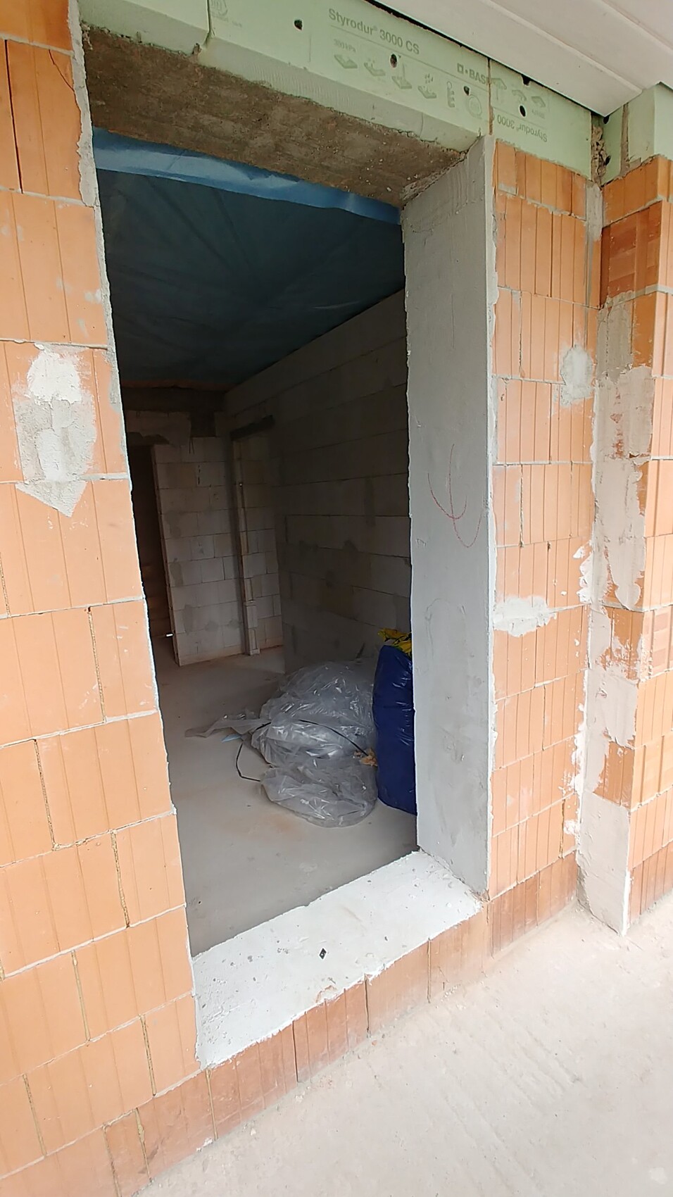 Construction site in shell stage: open door opening, brick walls, and building materials inside.