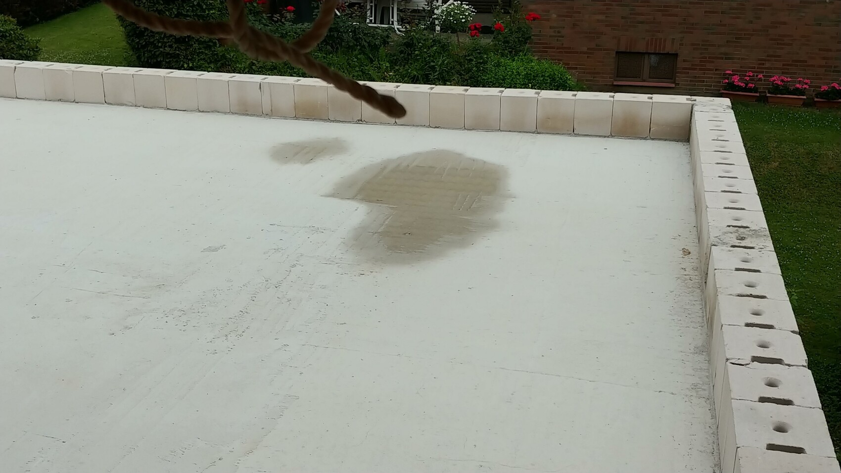 White flat roof terrace with wet spots and garden in the background