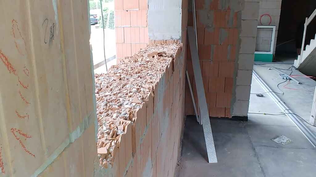 Construction site: incomplete brick wall with rubble on top, metal rod leaning against the wall.