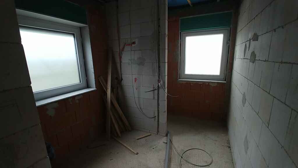 Unfinished basement room with two windows, stacks of wood and loose cables.