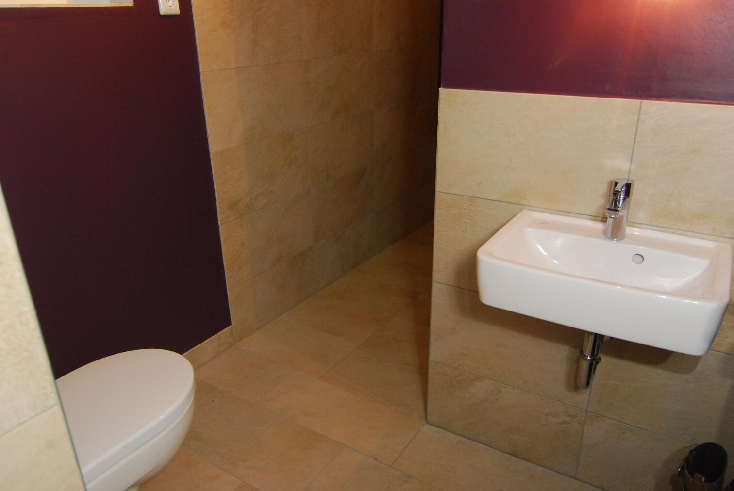 Bathroom with white wall-mounted washbasin on the right, toilet on the left, beige tiles, dark purple wall.