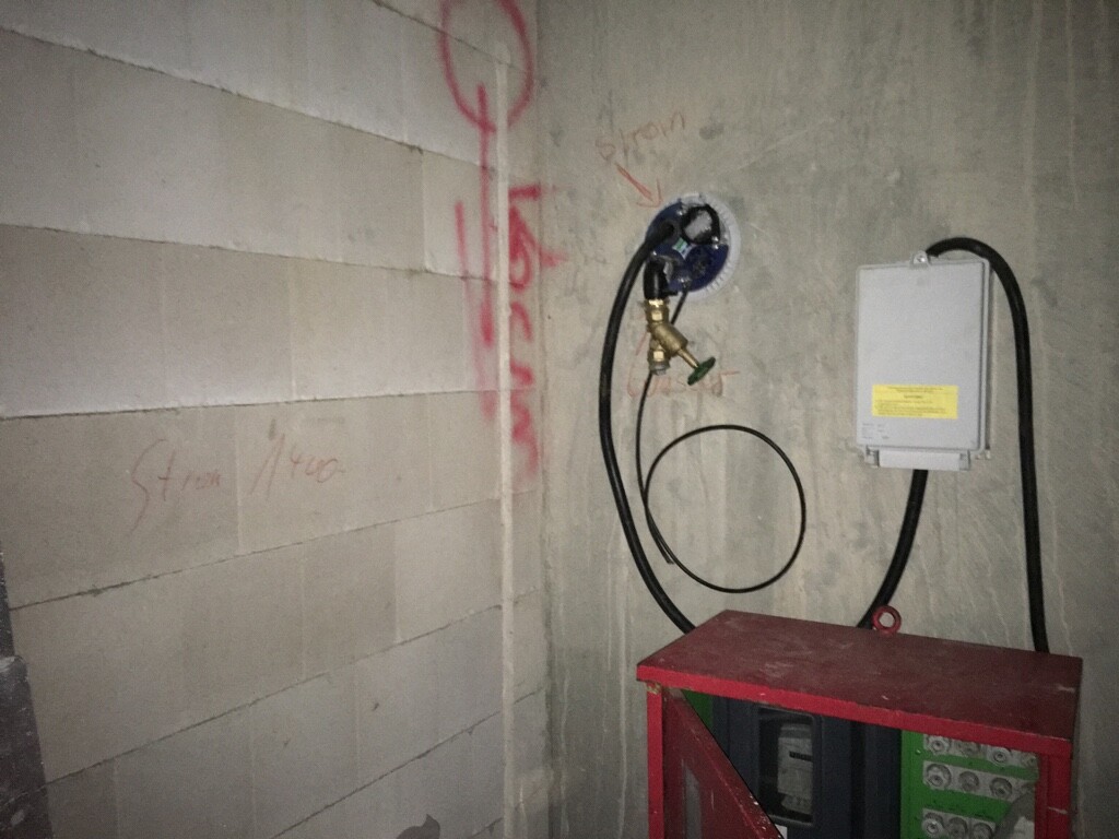 Shell construction site: electrical distribution box, cables, water connection on concrete wall.