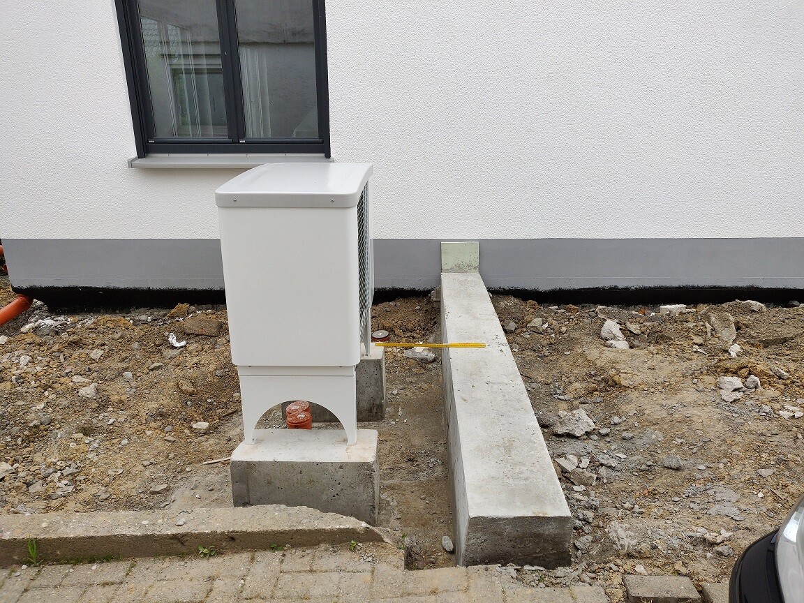 Outdoor condenser of a heating/air conditioning system installed on building ground in front of the house wall