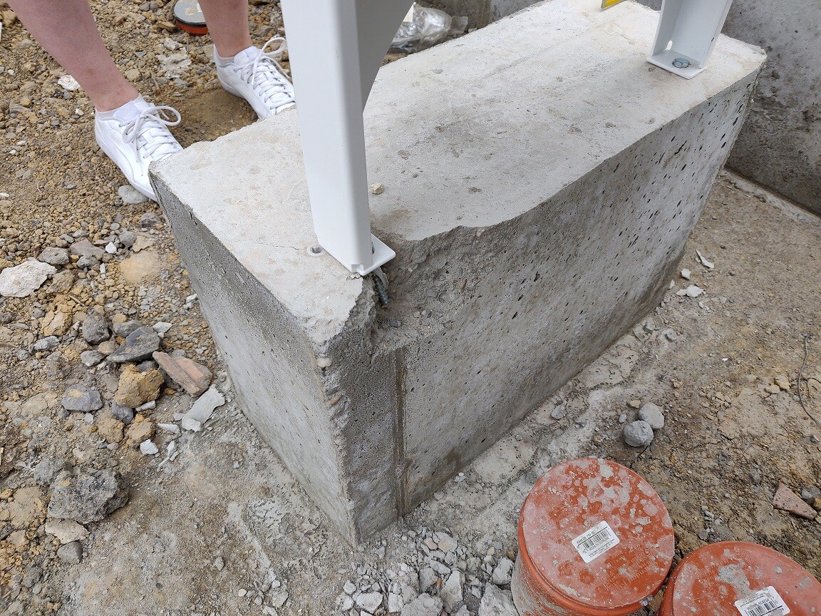 Large concrete foundation with mounted metal posts on a construction site and gravel around it.