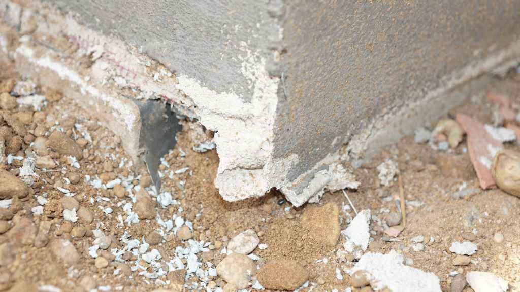 Damaged foundation on a concrete wall with soil and debris.