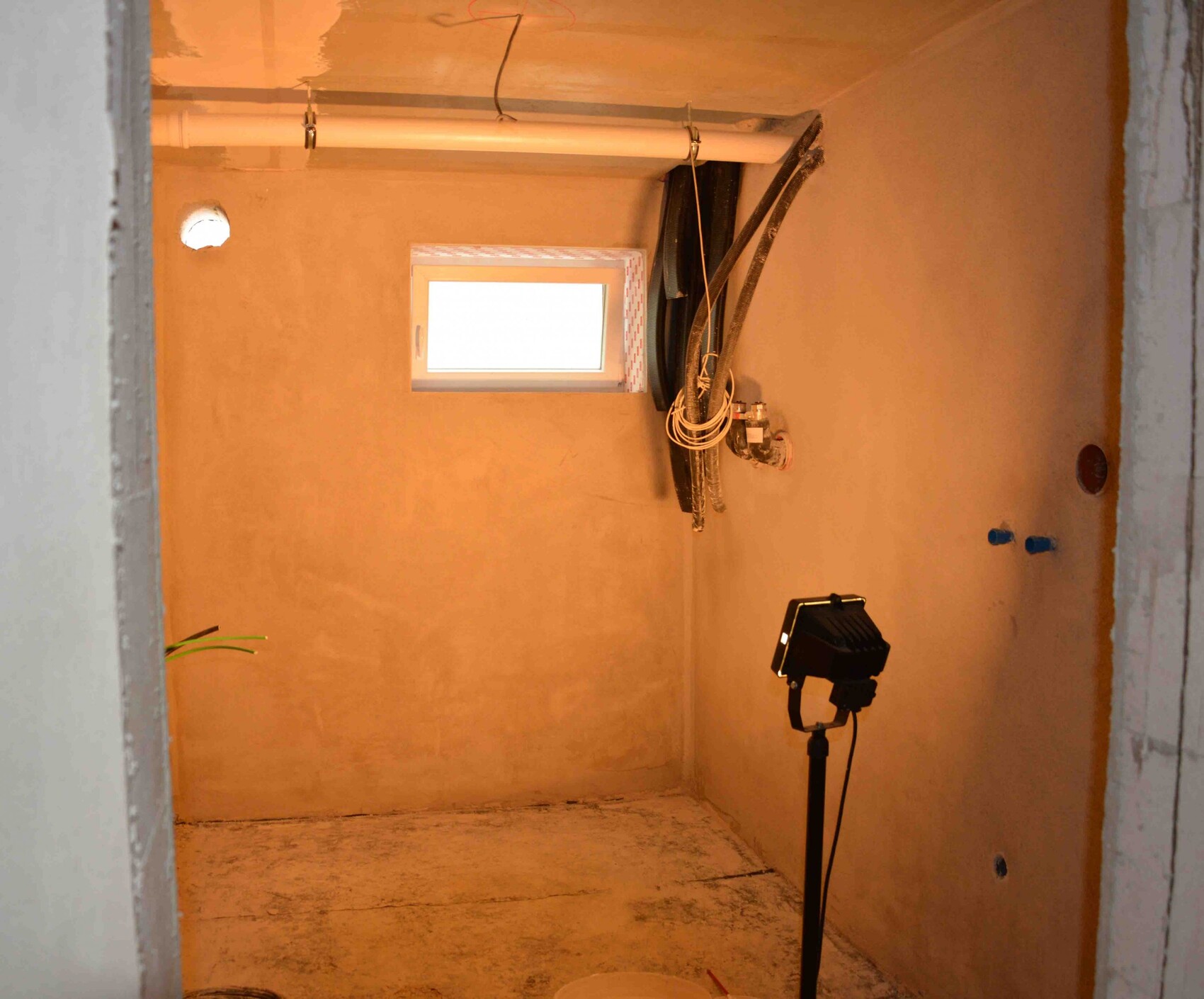 Small shell room with water pipes, cables, and construction lighting.