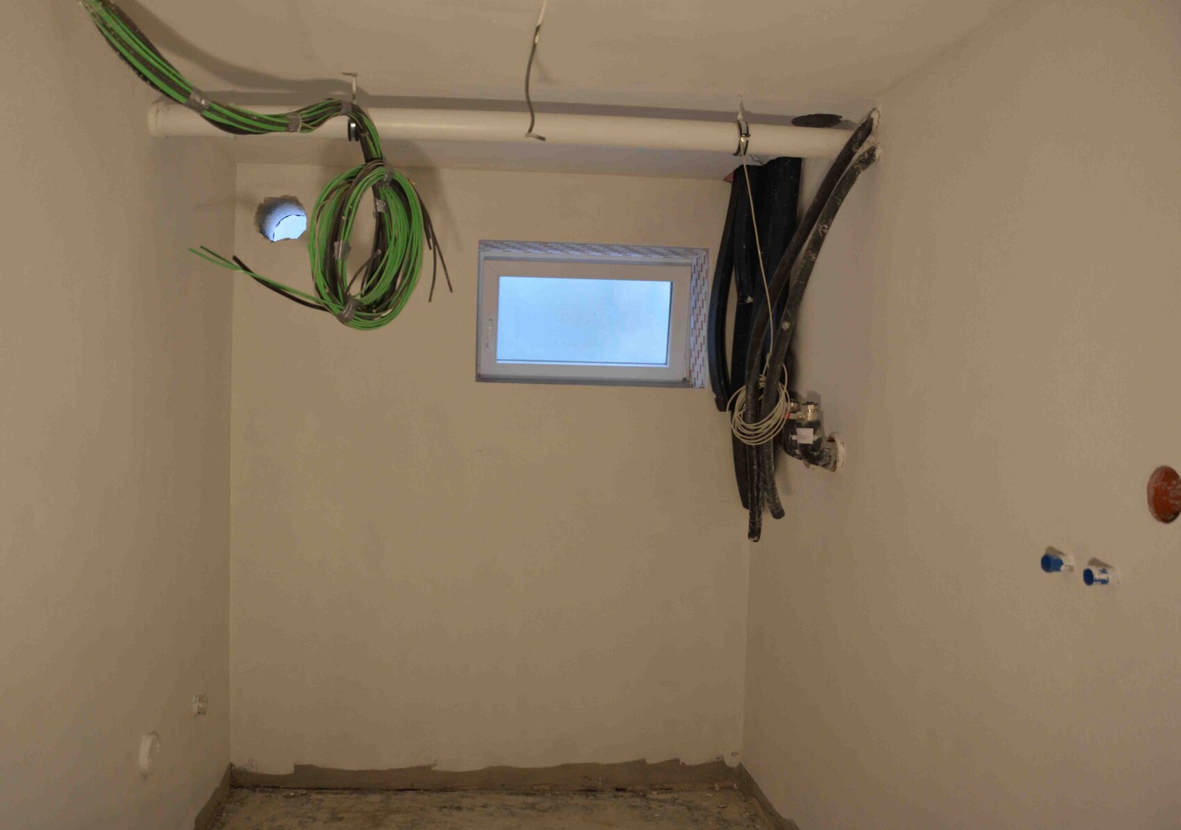 Construction room with cables, pipes, and a small window during the building process