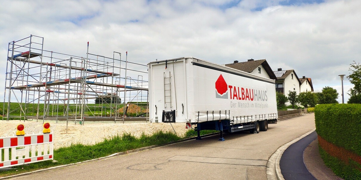 Construction site with scaffolding, TALBAUHAUS company truck trailers in front of residential houses