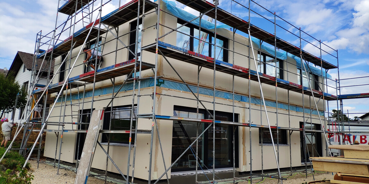 New house under construction with scaffolding, workers working on the facade.