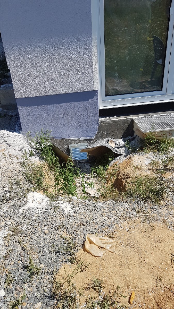 Außenwand eines Hauses mit freigelegtem Fundament, Baugrube, Kies und Unkraut