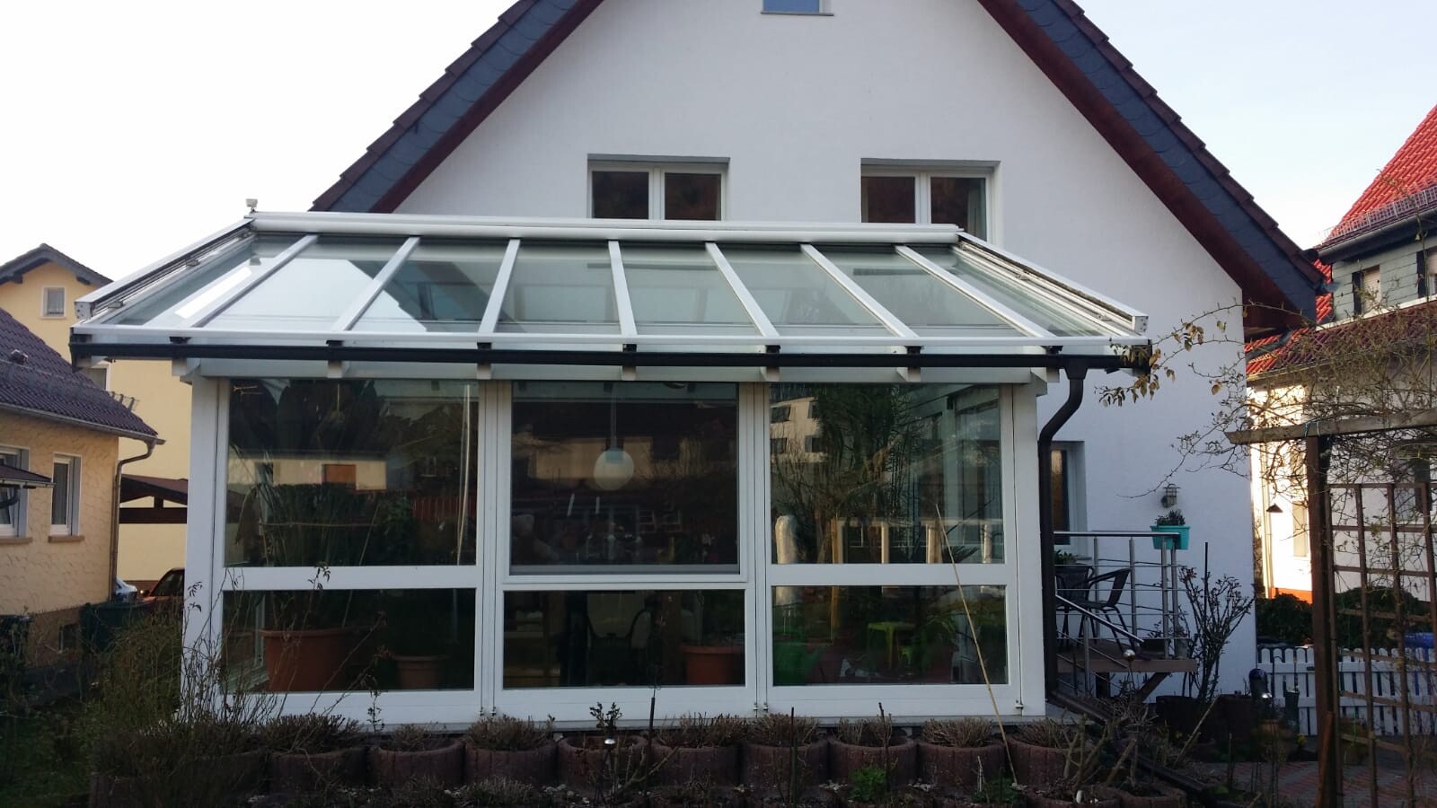 Exterior view of a house with glass veranda as conservatory in the garden, surrounded by plants