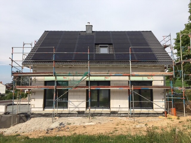 Detached house under construction with scaffolding all around and solar panels on the roof.