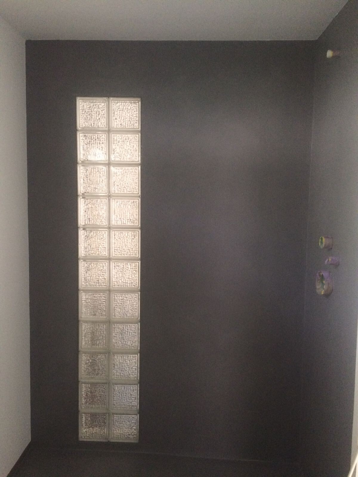 Dunkler Innenraum mit einer vertikalen Reihe Glasbausteine links; rechte Wand mit Anschlüssen.